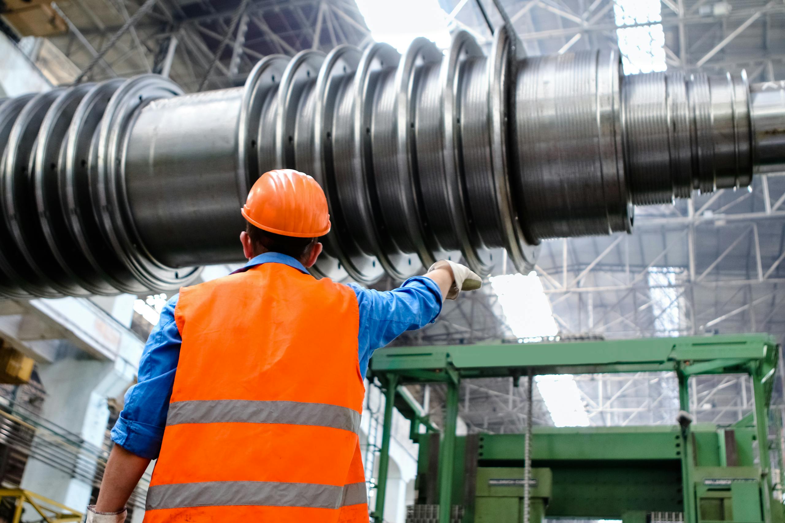 Engineer in high visibility vest and hard hat inspecting large machinery in factory setting.