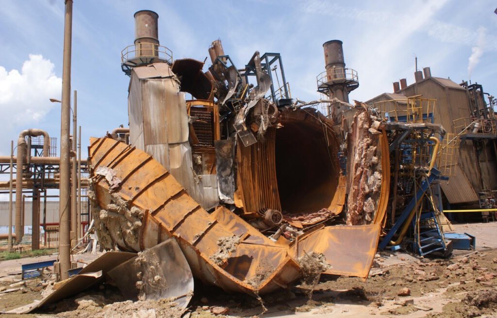 A low angle view of a rusty old industrial structure with pipes and beams against a clear blue sky.